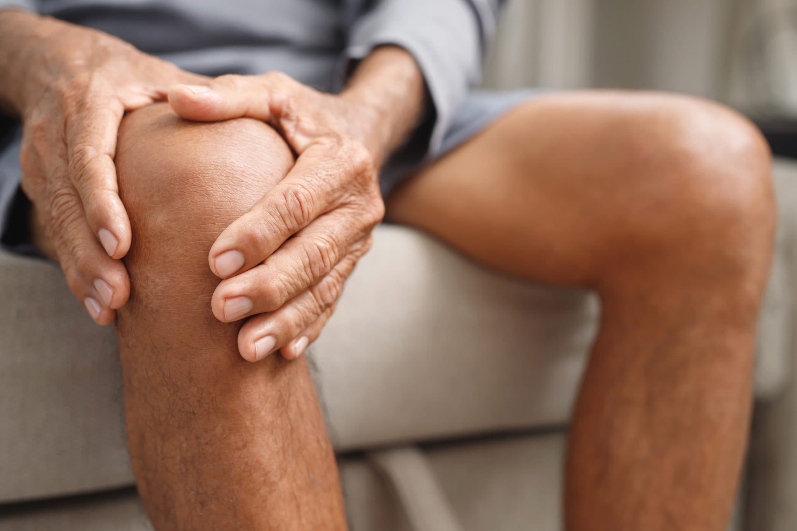 Senior man holding painful knee at home