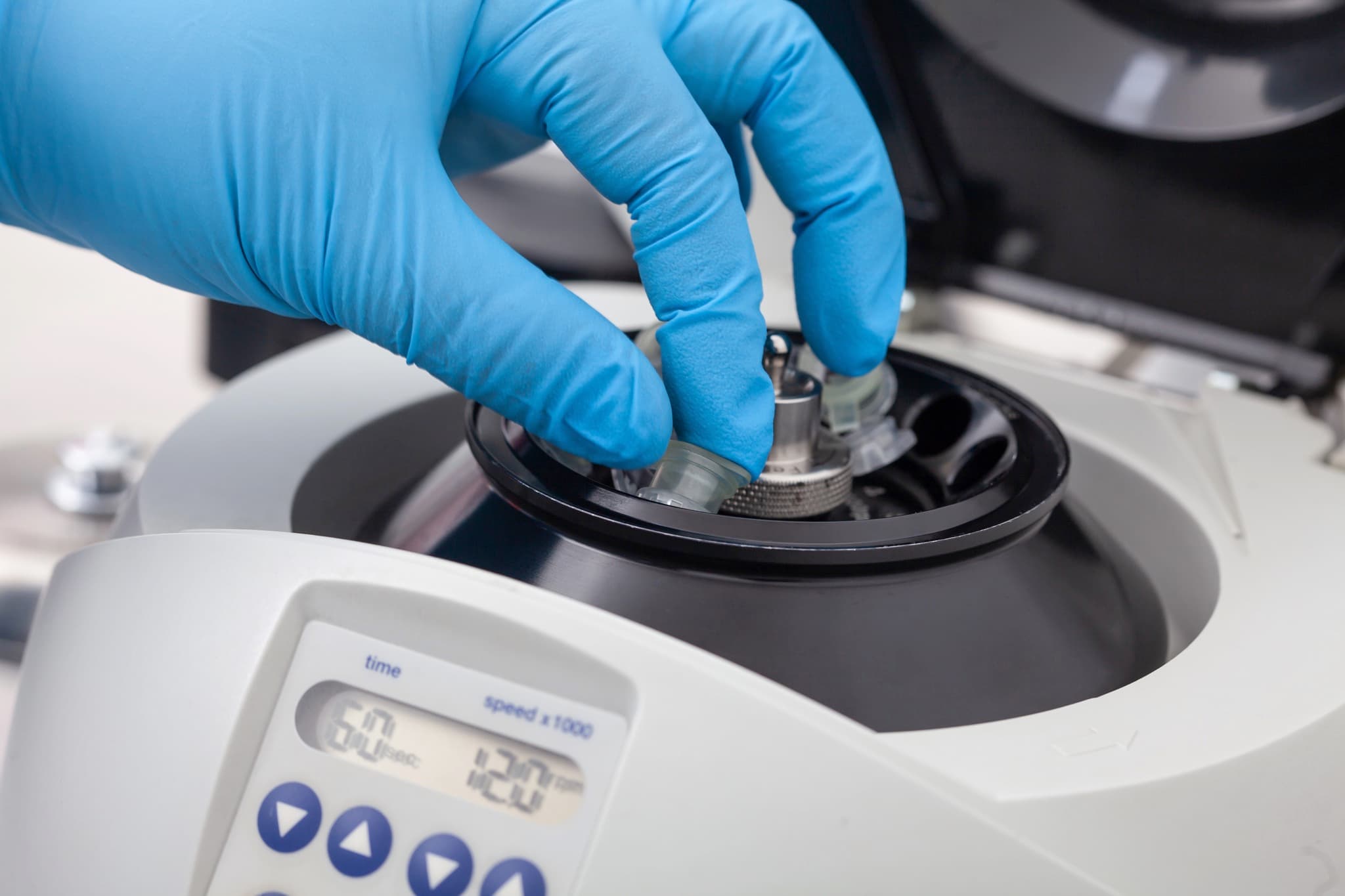 Blue-gloved hand loading tube into centrifuge rotor